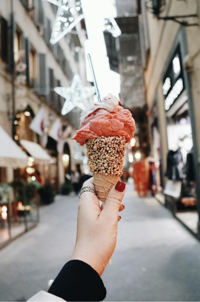 A woman with red nails is holding out a cone filled with Italian gelato